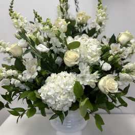 White floral arrangement in a white vase with roses, hydrangeas, and snapdragons
