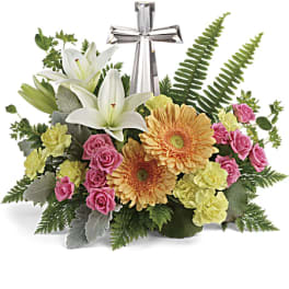 Floral arrangement with white lilies, pink roses, and orange gerbera daisies topped by a silver cross