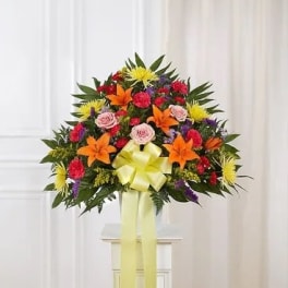 Colorful standing floral spray with lilies, roses, and a yellow ribbon