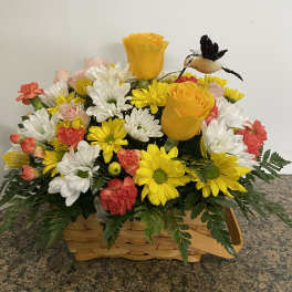 Basket arrangement of yellow and white daisies with pink roses and a small bird ornament