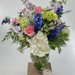 Mixed bouquet of pink roses, blue flowers, and white hydrangeas in a glass vase
