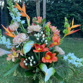 Tropical floral arrangement with orange birds of paradise and coral blooms in a green vase