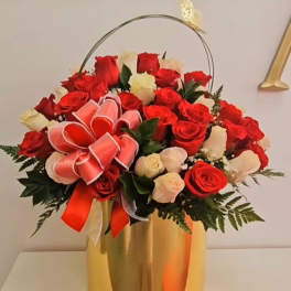Arrangement of red and white roses in a tall gold vase with a ribbon bow and butterfly accent