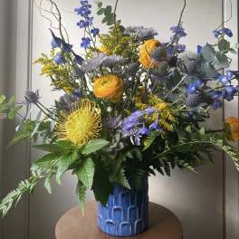 Tall mixed bouquet in a blue vase with yellow, blue, and lavender flowers