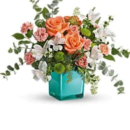 Peach roses and pink carnations in a turquoise glass vase