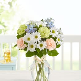 Bouquet of white daisies, pale carnations, and blue flowers in a glass vase