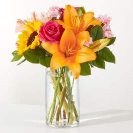Bouquet of orange lilies, a pink rose, and a sunflower in a glass vase