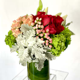 Red roses and peach blooms in a green glass vase with silver foliage