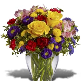 Mixed bouquet of yellow roses, purple asters, red carnations in a clear glass vase