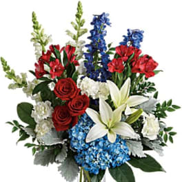 Bouquet of red roses, white lilies, blue hydrangeas, and tall blue and white spikes in a glass vase