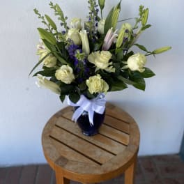 Bouquet of cream roses and lilies in a dark vase with a white ribbon