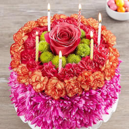 Round floral cake with lit candles and a central pink rose