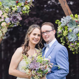 Bride and groom holding a bouquet in front of a floral arch