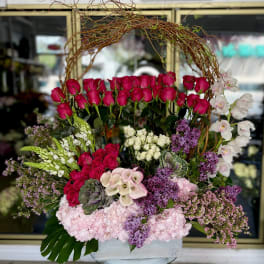 Large floral arrangement with pink roses, orchids, and purple blooms in a white container