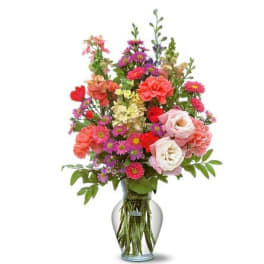 Tall mixed bouquet of pink roses, carnations, and purple asters in a clear glass vase