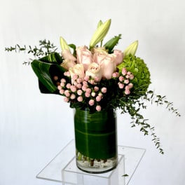 Pink roses and lilies arranged in a glass vase with green hydrangea