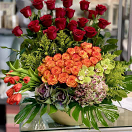 Mixed bouquet of red and orange roses with orchids in a low vase