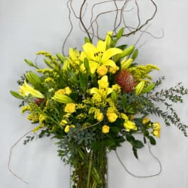 Yellow lilies and roses in a tall glass vase with curly branches