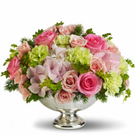 Low pastel arrangement of pink roses, green carnations, and hydrangeas in a silver pedestal bowl