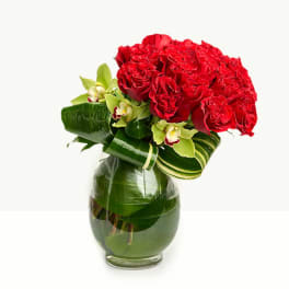 Red roses and green orchids arranged in a glass vase