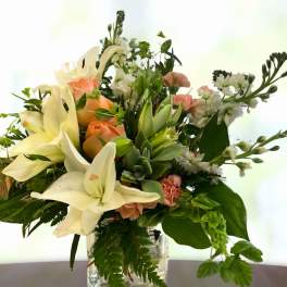 Bouquet of white lilies, peach roses, and white filler flowers in a glass vase