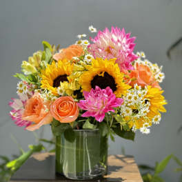 Bright mixed bouquet with sunflowers, roses, and daisies in a glass vase