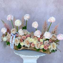 Long floral arrangement of pale roses and ranunculus in a wood container