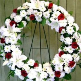 Heart-shaped floral wreath with white flowers and red roses on a stand