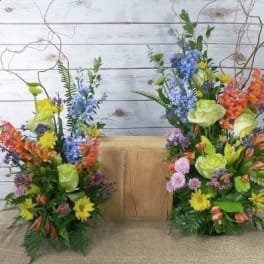 Two colorful floral arrangements flank a wooden box on burlap
