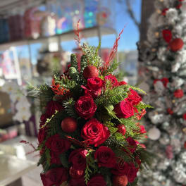 Red roses arranged with evergreen and red ornaments in a red container