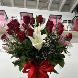 Tall bouquet of red roses and white lilies in a glass vase with a red ribbon