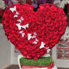 Heart-shaped arrangement of red roses with butterfly decorations on a white stand