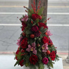 Christmas tree-shaped floral arrangement with red roses and pink orchids in a white pot