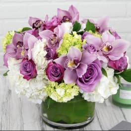 Pink orchids and roses arranged in a green glass vase