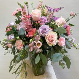 Pink and lavender rose bouquet in a glass vase with a butterfly pick