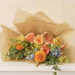 Bouquet of peach and yellow flowers wrapped in tan paper