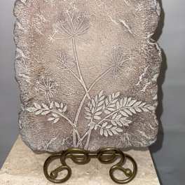 Textured stone plaque with an etched floral stem design on a metal stand