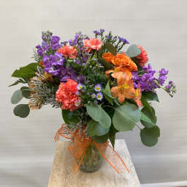 Mixed bouquet of purple, orange, and coral flowers in a glass vase
