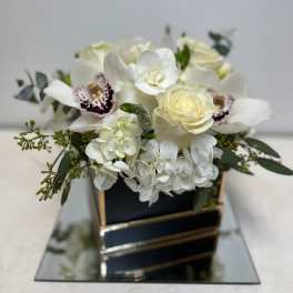 White roses and orchids arranged in a black box with gold trim