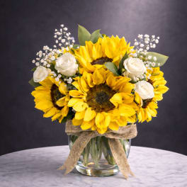 Sunflower and white rose bouquet in a glass vase with a burlap ribbon
