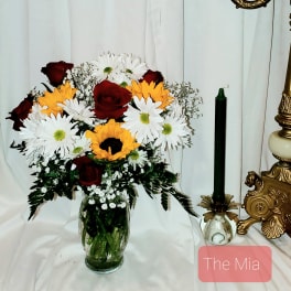 Bouquet of red roses, white daisies, and yellow sunflowers in a glass vase
