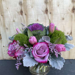 Pink roses and tulips arranged in a glass vase with silver foliage