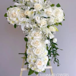 White floral cross arrangement on an easel with roses and lilies