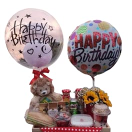 Birthday gift tray with balloons, teddy bear, snacks, and sunflowers