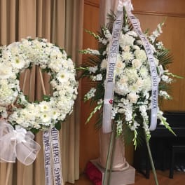 Two white funeral flower wreaths with condolence ribbons on stands
