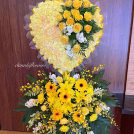 Heart-shaped yellow floral tribute above a mixed yellow standing spray