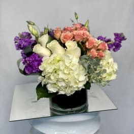 Mixed bouquet of roses, hydrangeas, and purple blooms in a glass vase
