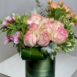 Pink roses arranged in a green cylindrical vase with mixed greenery
