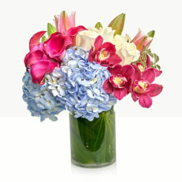 Bouquet of blue hydrangeas, pink calla lilies, and orchids in a glass vase
