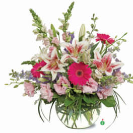 Round glass vase with pink lilies, bright pink gerbera daisies, and pastel blooms in a loose arrangement